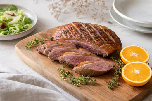 Skivat ankbröst med krispigt skinn och rosa kött på en skärbräda med timjan och apelsin