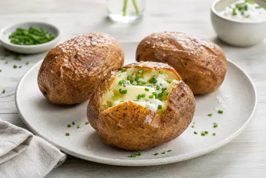 Bakad potatis med krispigt skal, delad på mitten och fylld med smör, gräddfil och gräslök