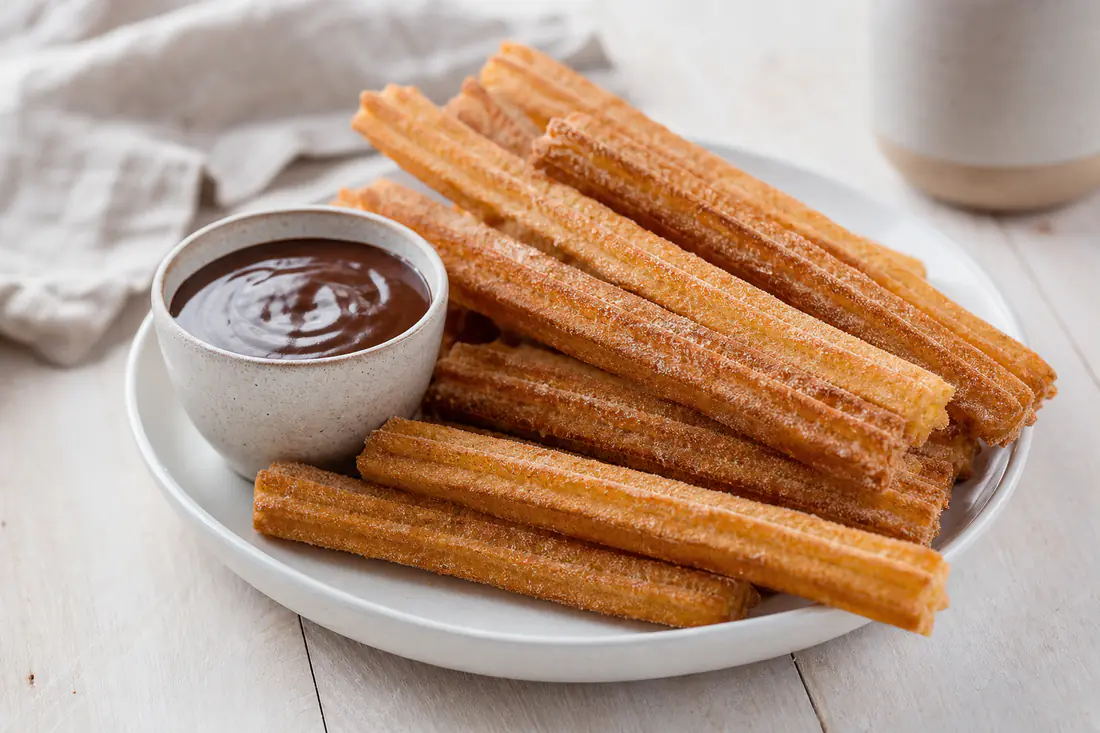 Räfflade gyllene churros rullade i kanelsocker bredvid en liten skål med varm chokladsås