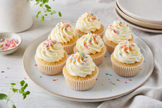 Vaniljcupcakes med vit smörkräm och färgglatt strössel på ett fat