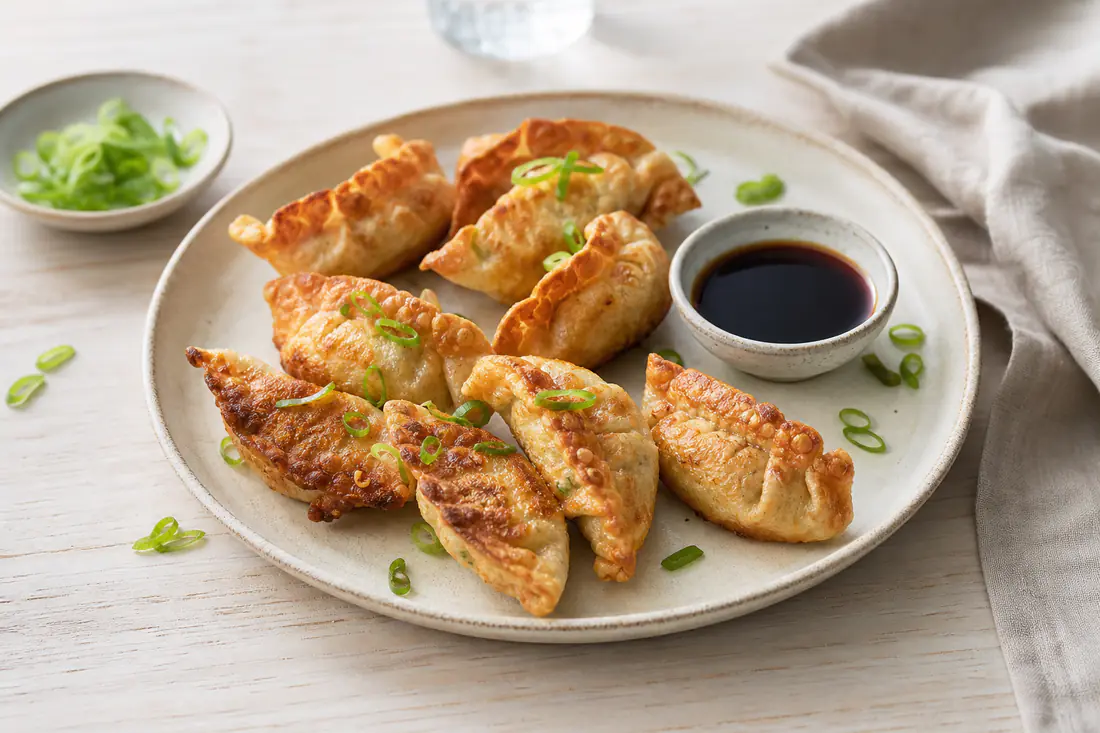Gyllene, krispiga dumplings på ett fat med en skål sojadippsås och strimlad salladslök