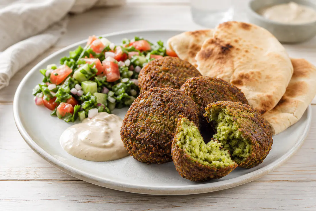 Krispiga falafel med grön insida på en tallrik med tahinisås, sallad och pitabröd