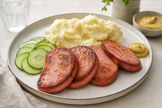 Stekta falukorvsskivor med brynt yta på en tallrik med potatismos, senap och skivad gurka
