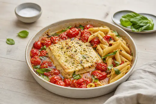 Bakad fetaost med sprucken cherrytomat och olivolja i en liten form, blandad med pasta och basilika