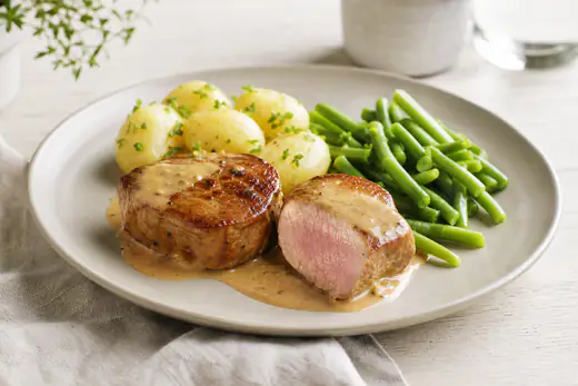 Gyllene fläskfilébiffar på en tallrik med kokt potatis, gräddsås och gröna bönor