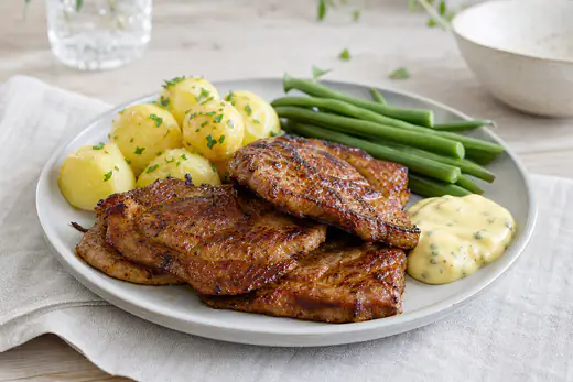 Marinerade och brunstekta flintasteksskivor på en tallrik med kokt potatis, gröna bönor och en klick bearnaisesås
