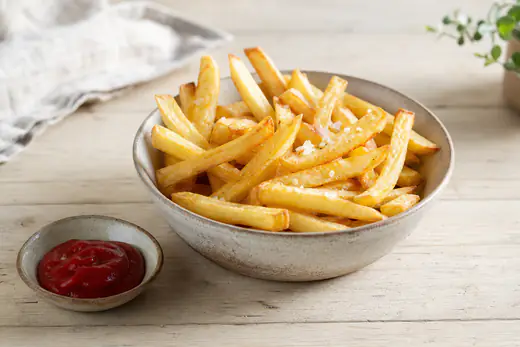 Gyllene krispiga pommes frites med flingsalt i en skål bredvid en liten skål ketchup