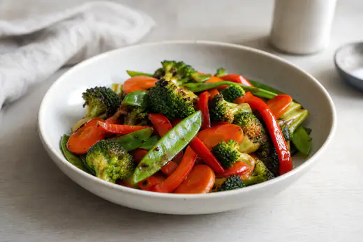 Stekta wokgrönsaker med broccoli, morötter, paprika och sockerärtor i en skål med lätt rostade kanter