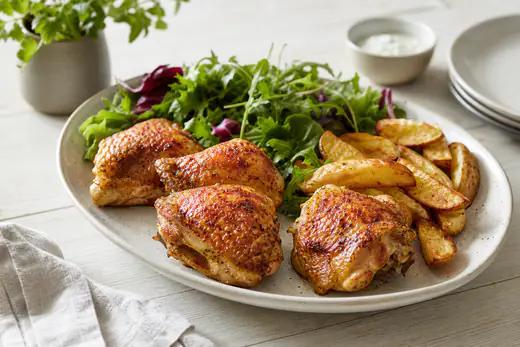 Fyra gyllene kycklinglår med krispigt paprikakryddat skinn på ett fat med klyftpotatis och sallad