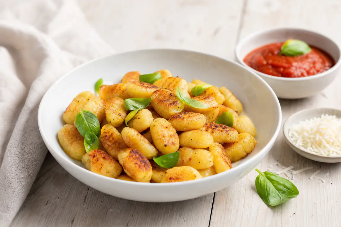 Gyllene krispiga gnocchi i en skål med basilika och en liten skål tomatsås bredvid