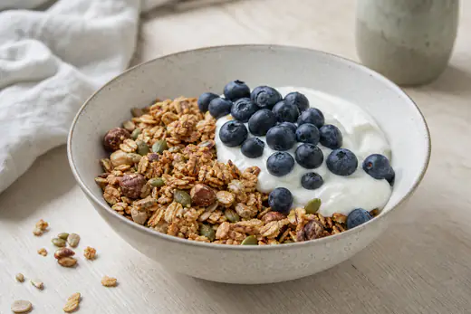 Gyllene hemgjord granola med nötter och frön i en skål, serverad med yoghurt och bär