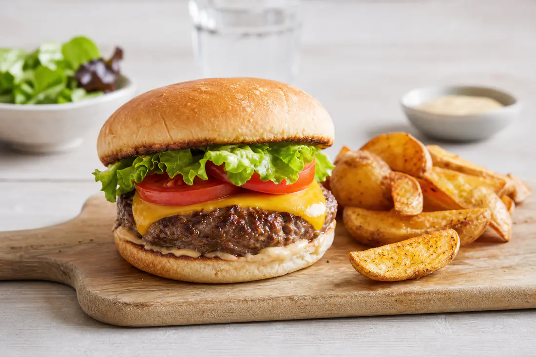 Hamburgare med nötbiff, smält ost, sallad och tomat i ett lätt rostat bröd, serverad med klyftpotatis