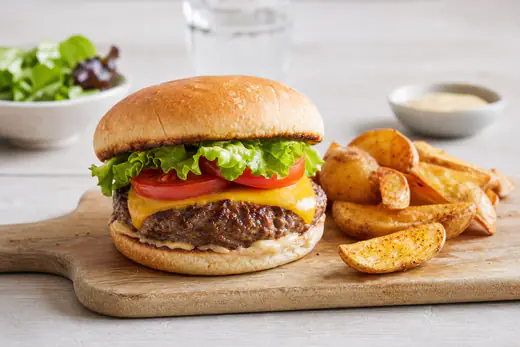 Hamburgare med nötbiff, smält ost, sallad och tomat i ett lätt rostat bröd, serverad med klyftpotatis