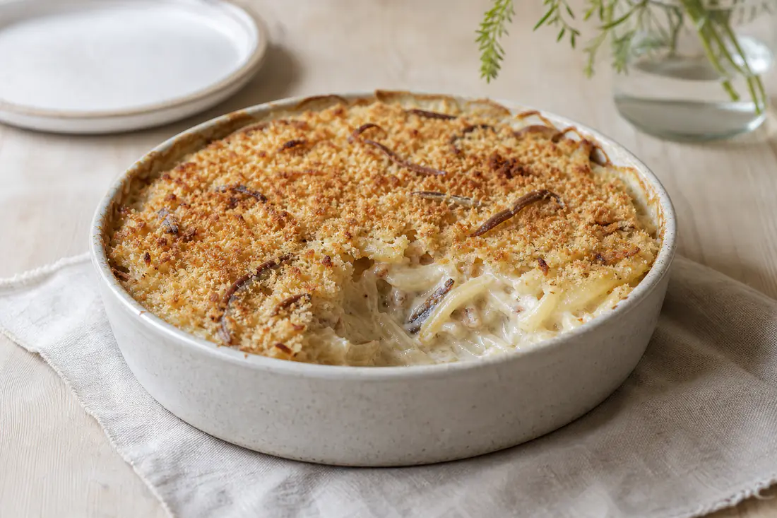 Janssons frestelse med gyllene brödsmulor i en liten rund form, en portion urtagen med potatisstrimlor, lök och ansjovis i krämig sås