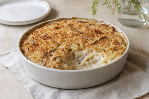 Janssons frestelse med gyllene brödsmulor i en liten rund form, en portion urtagen med potatisstrimlor, lök och ansjovis i krämig sås