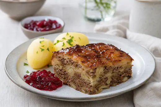 Skiva av kålpudding med brunad köttfärs och karamelliserad vitkål på en tallrik med kokt potatis och lingonsylt