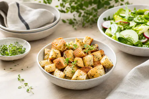 Gyllene brödkrutonger med örter i en skål bredvid en grön sallad