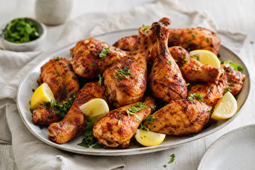 Krispiga kycklingben med paprikakrydda på ett fat med citronklyftor och persilja