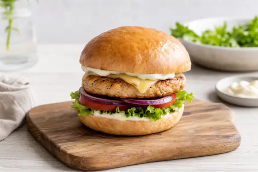 Kycklingburgare med gyllene biff, sallad, tomat, rödlök och majonnäs i ett rostat hamburgerbröd på en träbricka