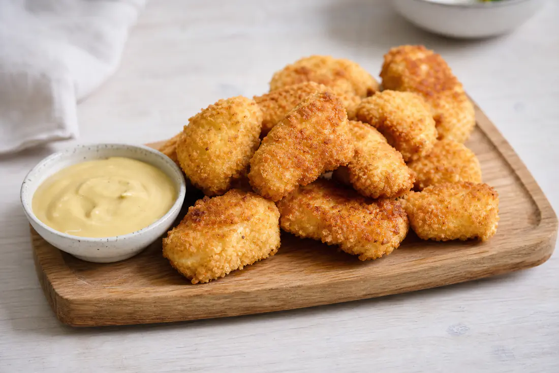 Gyllene hemgjorda kycklingnuggets med pankopanering på ett bräde med en skål dippsås