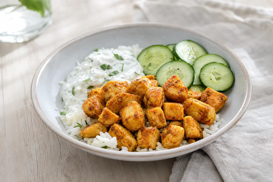 Gyllene, paprikakryddade kycklingtärningar i en skål med ris, gurka och en sked yoghurtsås