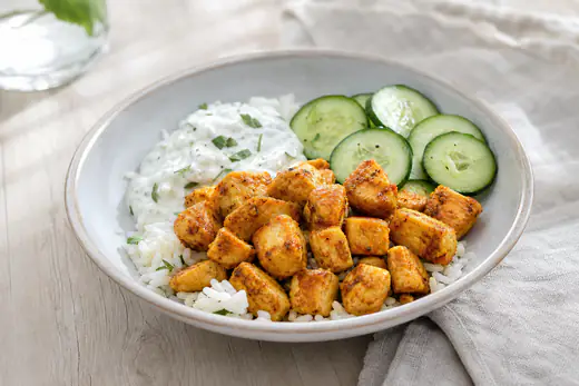 Gyllene, paprikakryddade kycklingtärningar i en skål med ris, gurka och en sked yoghurtsås