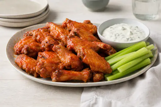Blanka buffalo wings i röd chilisås på ett fat med selleristänger och en skål ädelostdipp