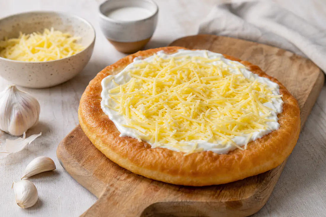 Gyllene runda langos med gräddfil och riven ost på en träbräda