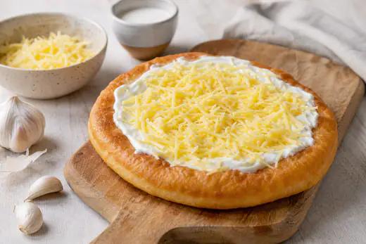 Gyllene runda langos med gräddfil och riven ost på en träbräda