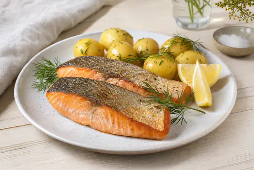 Två gyllene laxfiléer med skinn på en tallrik med citronklyftor, dill och kokt potatis