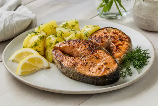 Två laxkotletter med ben på en tallrik med kokt potatis, dill och citronklyftor