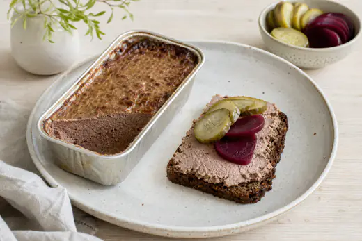 Hemgjord leverpastej i en liten aluminiumform med en skiva bredd på rågbröd med inlagd gurka och rödbetor