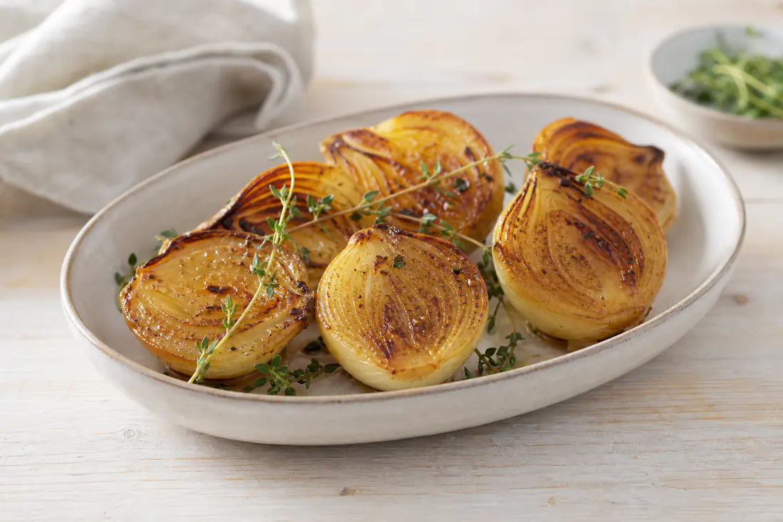 Rostade gula lökhalvor med karamelliserad snittyta och timjan på ett serveringsfat