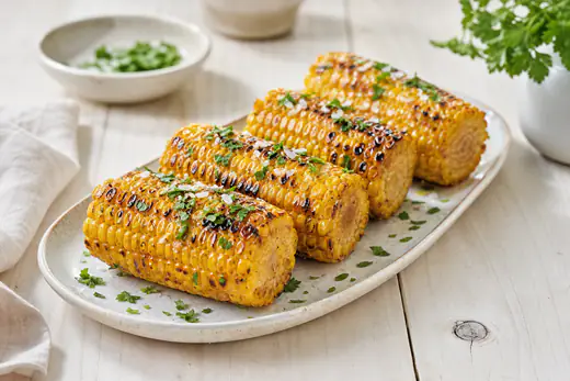 Grillade majskolvar med smält smör, flingsalt och hackad persilja på ett avlångt fat