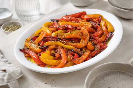 Rostade strimlor av röd, gul och orange paprika med svedda kanter på ett vitt fat