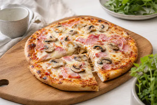 Liten rund pizza med skinka, champinjoner och smält mozzarella på en skärbräda, en bit utskuren