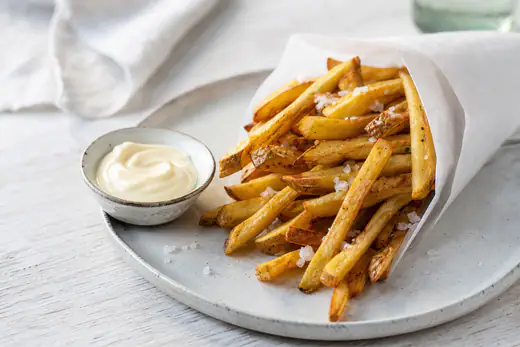 Gyllene hemgjorda pommes frites med flingsalt i en papperskorg med majonnäs bredvid
