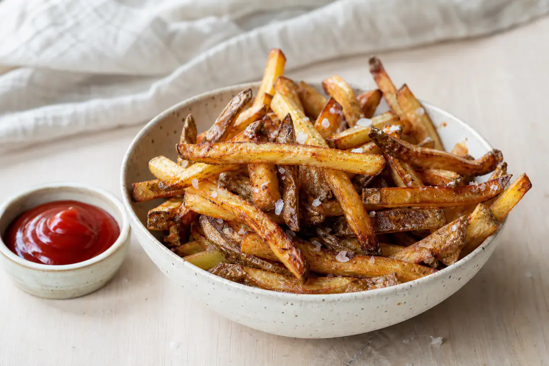 Hemmagjorda krispiga pommes med skal och flingsalt i en skål med en liten skål ketchup bredvid