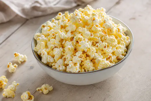 En skål nypoppade popcorn med smält smör och salt på ett träbord