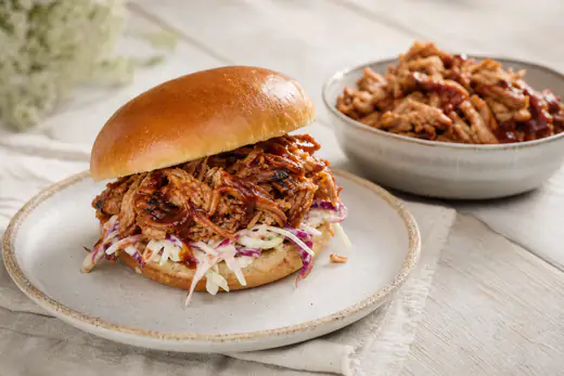 Tråddraget pulled pork med barbecuesås i ett briochebröd med coleslaw, mer kött i en skål bredvid