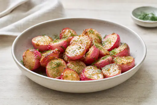 Halverade rostade rädisor med gyllene snittytor, smör och dill i en liten skål