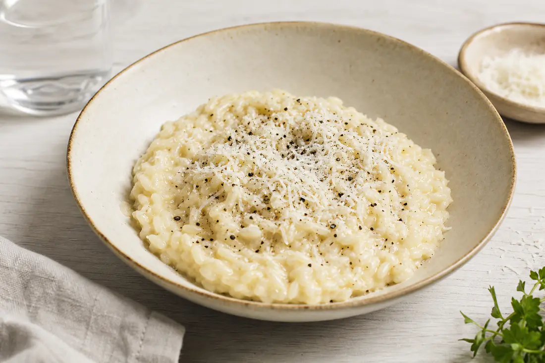 Krämig parmesanrisotto i en djup tallrik med nyriven parmesan och svartpeppar