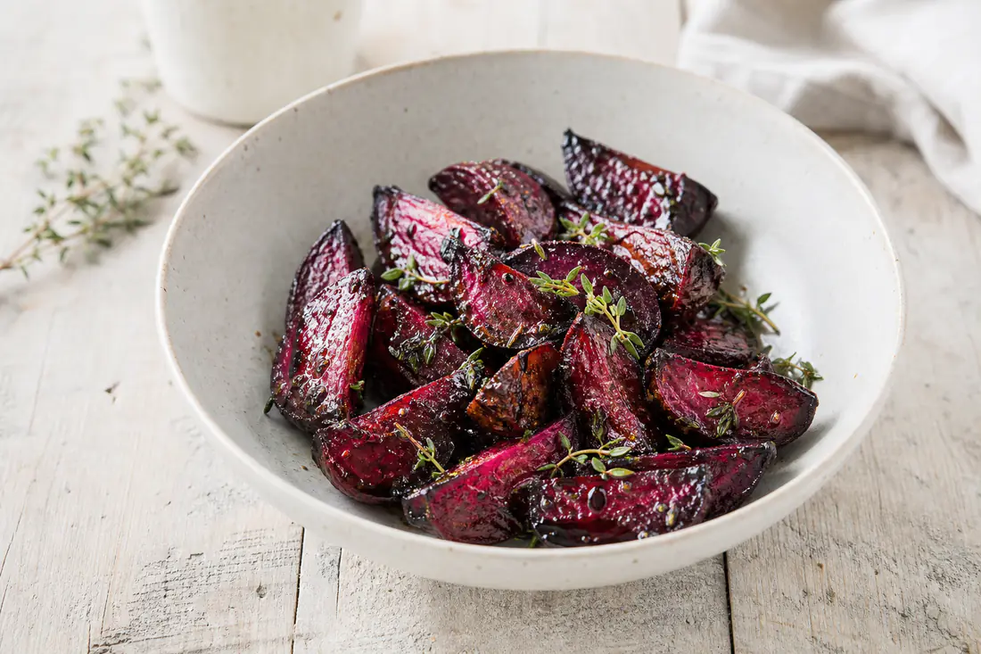 Rostade rödbetsklyftor med karamelliserade kanter i en skål, med timjan och en skvätt balsamvinäger