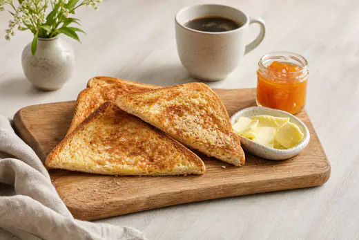 Gyllene rostade brödskivor på en skärbräda med smör, marmelad och en kopp kaffe