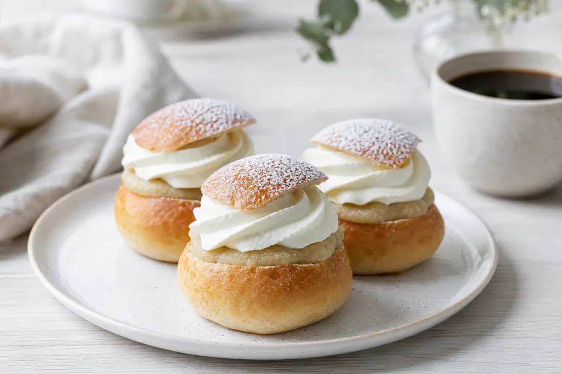 Semlor med vispgrädde, mandelmassa och ett lock av florsockerdammad vetebulle på ett fat