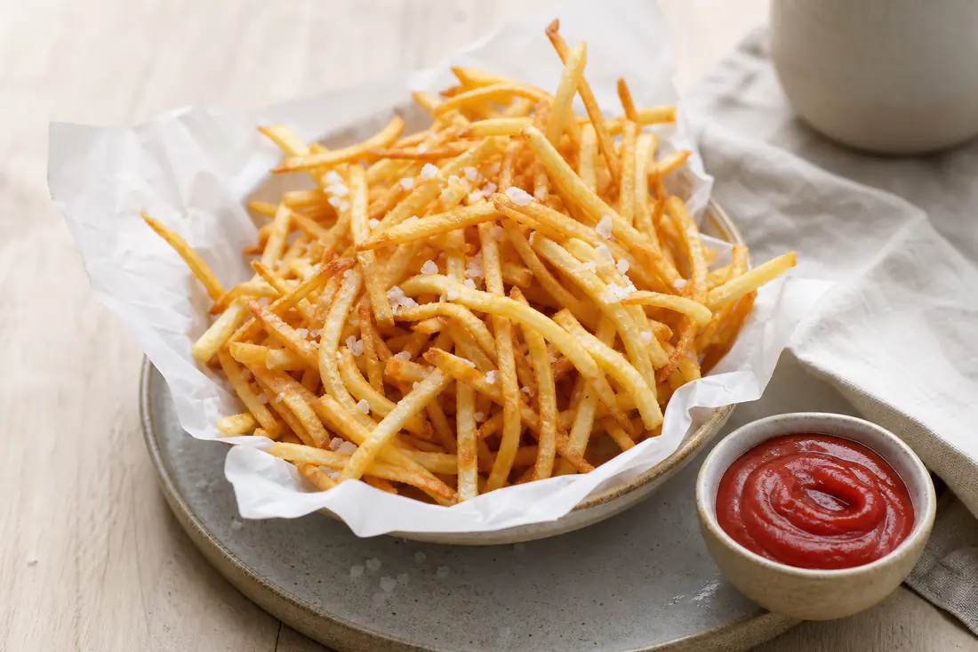 Tunna, gyllene pommes strips med flingsalt i en papperskorg med en skål ketchup bredvid