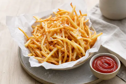 Tunna, gyllene pommes strips med flingsalt i en papperskorg med en skål ketchup bredvid