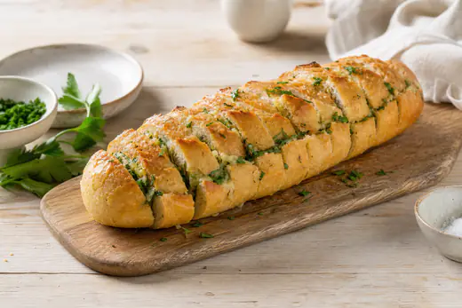 Gyllene vitlöksbröd på baguette med smält vitlökssmör och persilja på en skärbräda